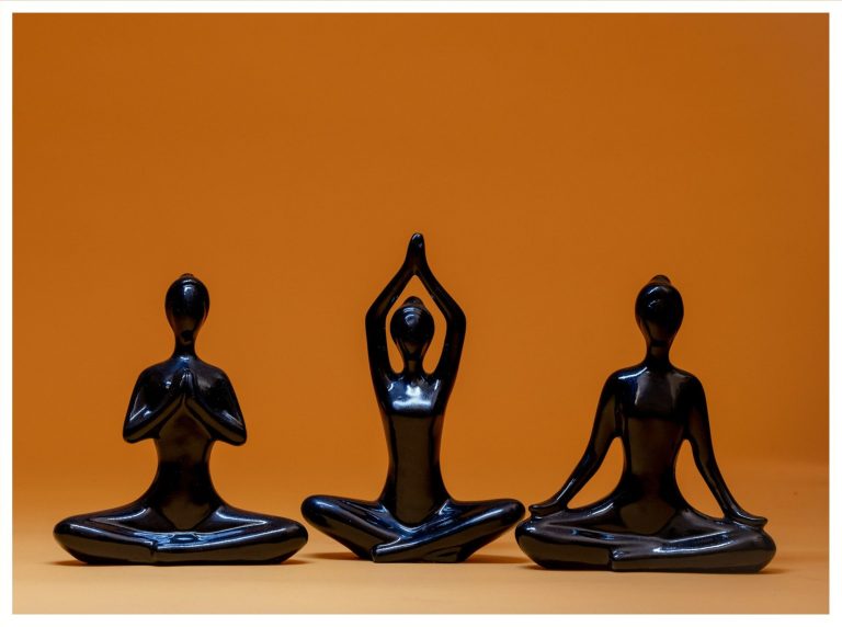 Yoga Drei schwarze Figuren in Yoga-Posen vor orangefarbenem Hintergrund.