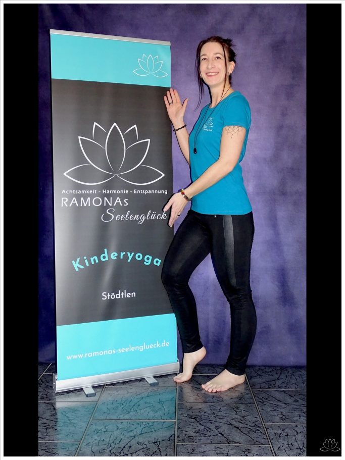 Lächelnde Frau in blauem T-Shirt und schwarzer Leggings, steht neben einem Banner.