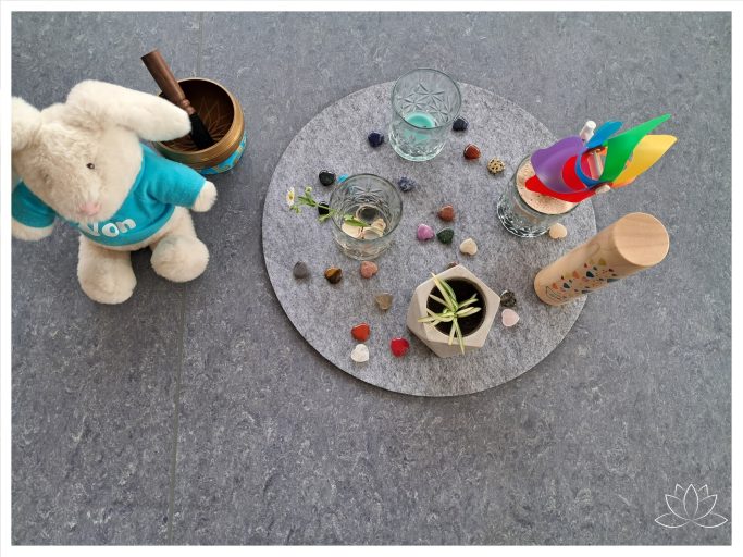 Teller mit bunten Objekten, Pflänzchen und einem Plüschtier in einer spiralförmigen Anordnung.