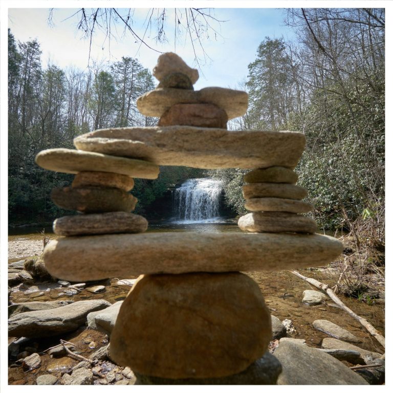 Steinerne Skulptur vor einem Wasserfall in einer bewaldeten Umgebung.